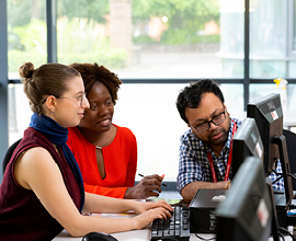 Two students sat at computer having a discussion with academics